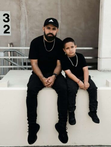 father and son sitting on a ledge, both wearing black.