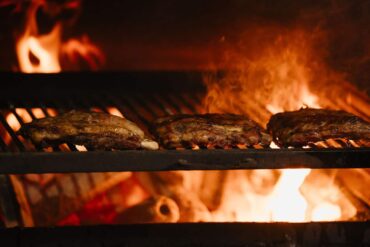 Close-up of Thai-style meats grilling over an open woodfire flame at Fi Woodfire Thai, the new Shaw Centre restaurant featuring 450°C lychee wood ovens.