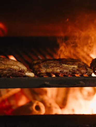 Close-up of Thai-style meats grilling over an open woodfire flame at Fi Woodfire Thai, the new Shaw Centre restaurant featuring 450°C lychee wood ovens.