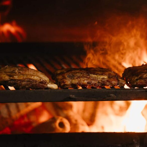 Close-up of Thai-style meats grilling over an open woodfire flame at Fi Woodfire Thai, the new Shaw Centre restaurant featuring 450°C lychee wood ovens.