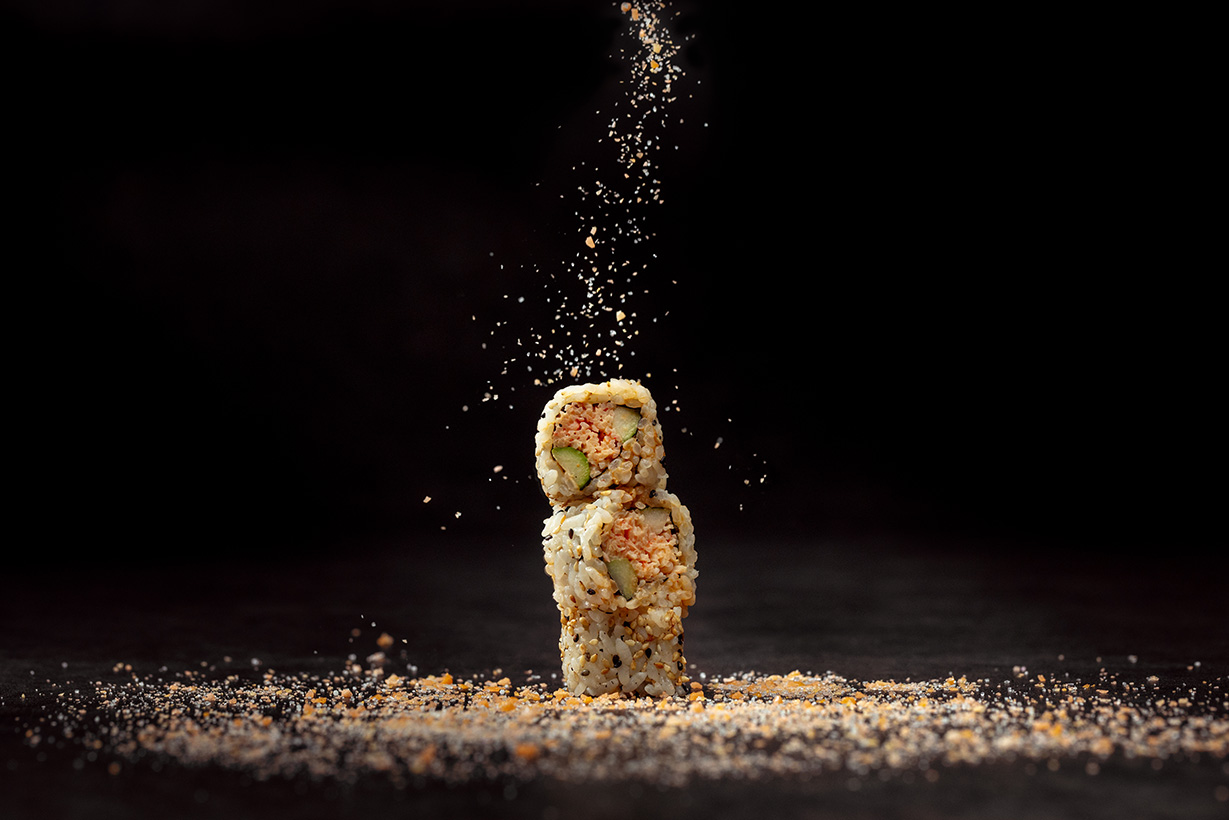 Close-up of Akira Back Singapore’s Pop Rockin’ maki roll with crab, avocado and popping candy, dramatically plated with seasoning falling mid-air.