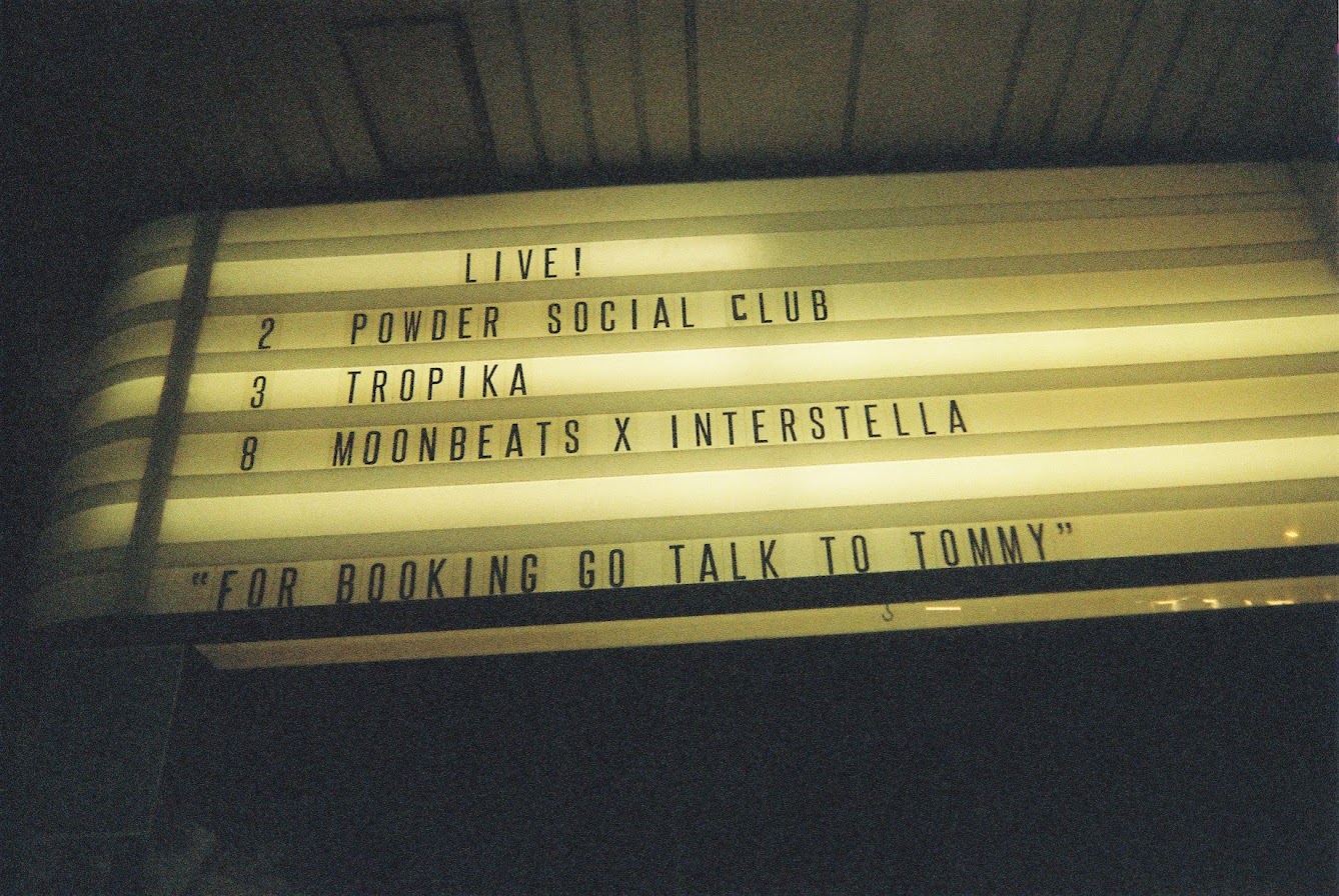 Illuminated marquee sign listing upcoming shows at The Projector, Singapore in 2019, including Powder Social Club, Tropika, and Moonbeats x Interstella. 
