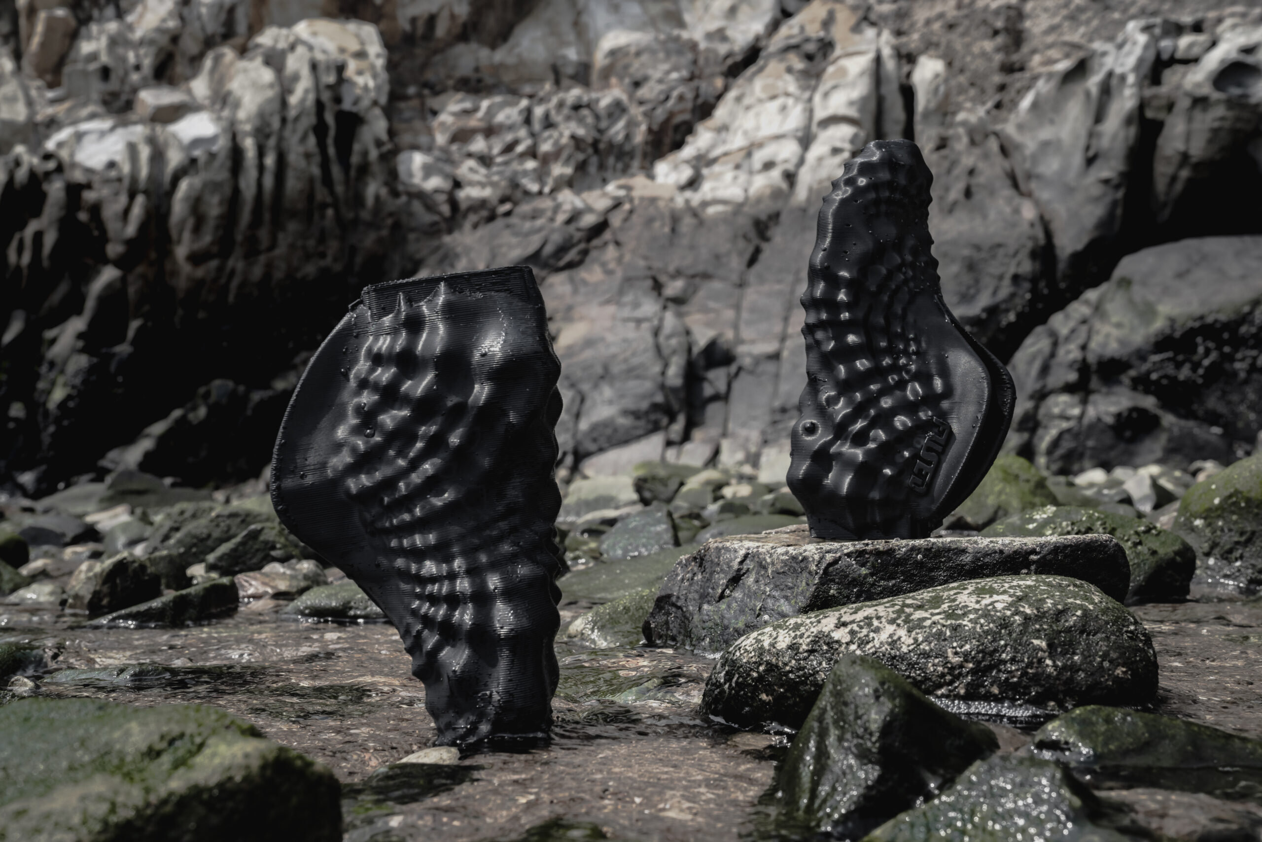 A pair of 3D-printed shoes displayed on rocks and water 