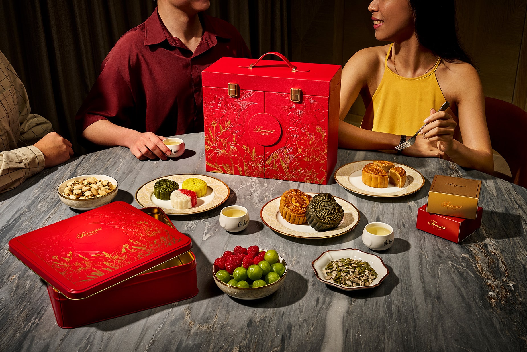 Fairmont Singapore’s 60th anniversary mooncake collection with red and gold gift box, assorted baked and snowskin mooncakes, and a tea-sharing moment between friends.