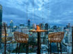 Rooftop table at Pastel Bangkok with rattan chairs overlooking the city skyline at dusk, capturing the Mediterranean-inspired atmosphere from above.