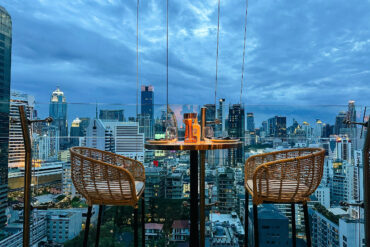 Rooftop table at Pastel Bangkok with rattan chairs overlooking the city skyline at dusk, capturing the Mediterranean-inspired atmosphere from above.