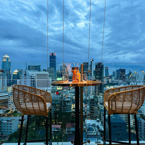 Rooftop table at Pastel Bangkok with rattan chairs overlooking the city skyline at dusk, capturing the Mediterranean-inspired atmosphere from above.