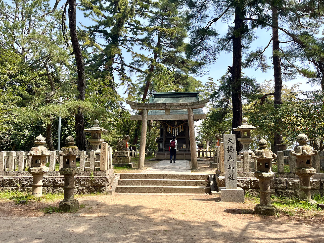 Entrance to Amanohashidate Shrine with stone lanterns and torii gate surrounded by pine trees in Miyazu, Kyoto, Japan.