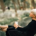 Confident older woman in black dress relaxing outdoors with a coffee, embodying grace, self-assurance, and healthy aging during menopause.