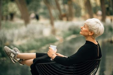 Confident older woman in black dress relaxing outdoors with a coffee, embodying grace, self-assurance, and healthy aging during menopause.