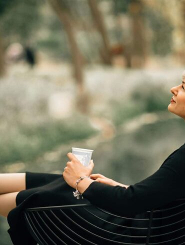 Confident older woman in black dress relaxing outdoors with a coffee, embodying grace, self-assurance, and healthy aging during menopause.