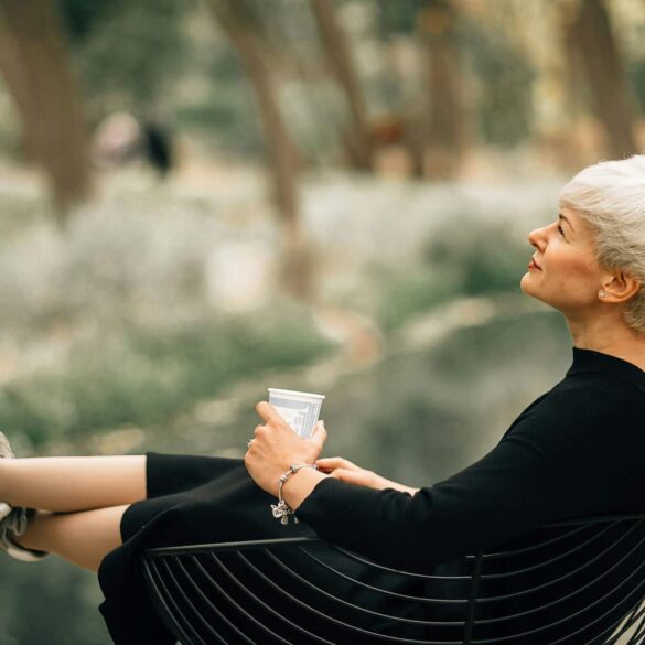 Confident older woman in black dress relaxing outdoors with a coffee, embodying grace, self-assurance, and healthy aging during menopause.