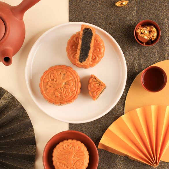 Traditional baked mooncakes served with Chinese tea in a Mid-Autumn Festival flat lay, featuring intricate gold fans, red teacups, and festive decor — perfect for celebrating the mooncake season in Singapore.