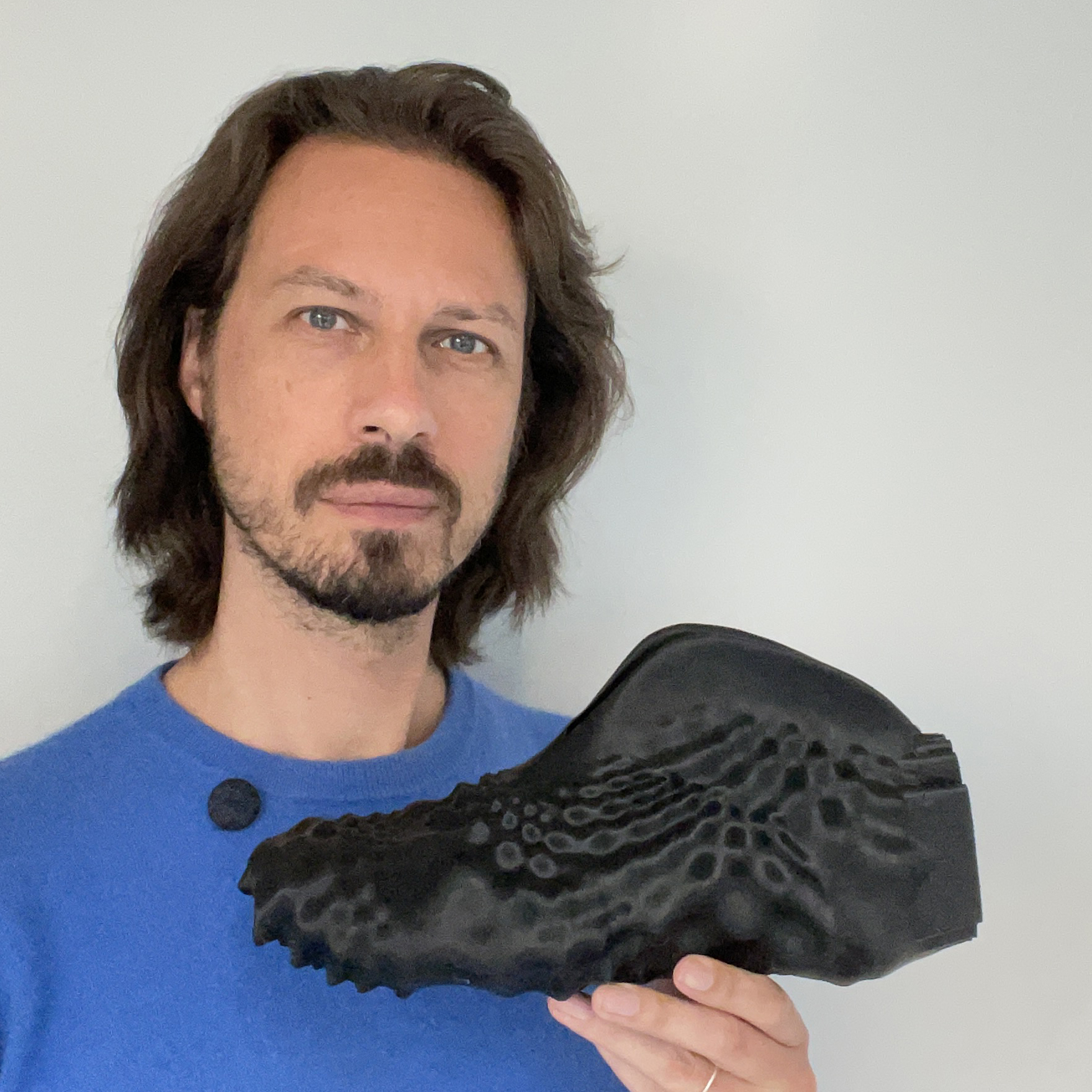 A caucasian male, wearing a blue shirt holding a futuristic 3D-printed shoe