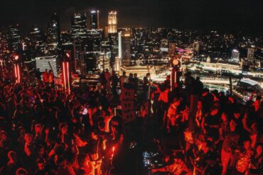 Crowd dancing at AFTER 2049 rooftop party at Marina Bay Sands SkyPark during F1 weekend in Singapore, with city skyline in the background.