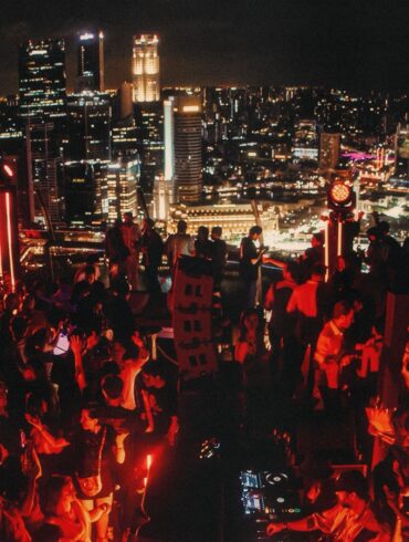 Crowd dancing at AFTER 2049 rooftop party at Marina Bay Sands SkyPark during F1 weekend in Singapore, with city skyline in the background.