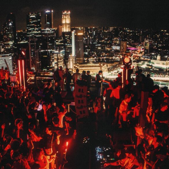 Crowd dancing at AFTER 2049 rooftop party at Marina Bay Sands SkyPark during F1 weekend in Singapore, with city skyline in the background.