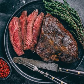 Grilled hanger steak served medium rare with fresh thyme and pink peppercorns on a black plate