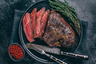 Grilled hanger steak served medium rare with fresh thyme and pink peppercorns on a black plate