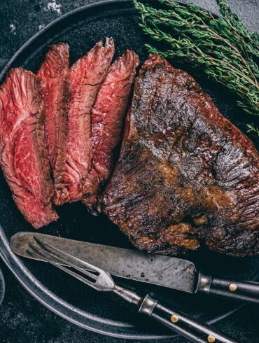 Grilled hanger steak served medium rare with fresh thyme and pink peppercorns on a black plate