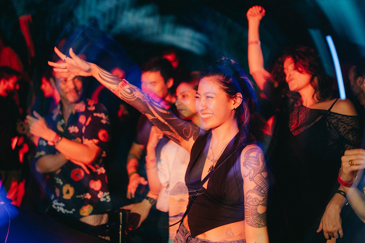 Tattooed partygoers dancing at Mandala Mansion’s F1 rooftop afterparty at HighHouse and NOVA, lit by immersive lighting installations.