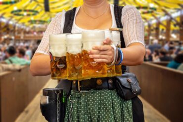Oktoberfest, Munich. Waiter in traditional Bavarian costume serving beers, close up view. October fest German beer festival.