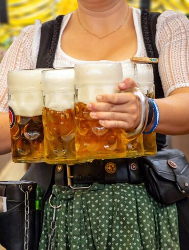 Oktoberfest, Munich. Waiter in traditional Bavarian costume serving beers, close up view. October fest German beer festival.