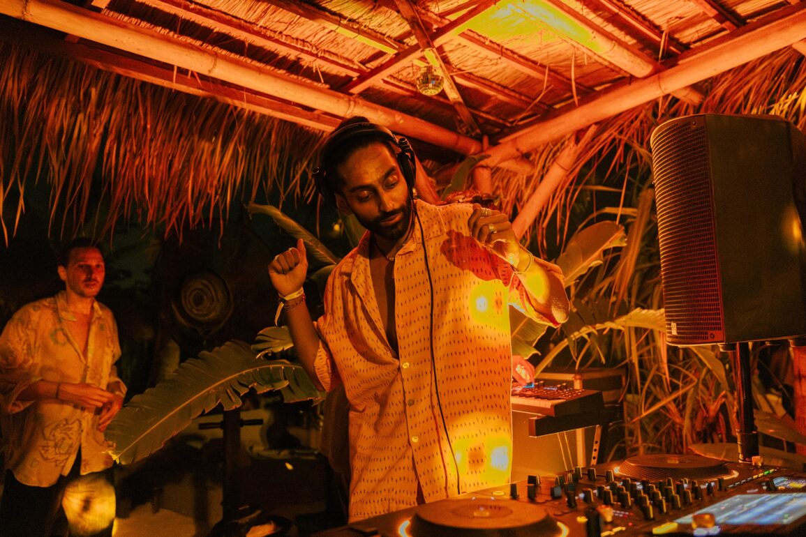 DJ HIMMAT performing in Bali under warm amber lights, immersed in tropical surroundings while spinning organic house and world electronic music.