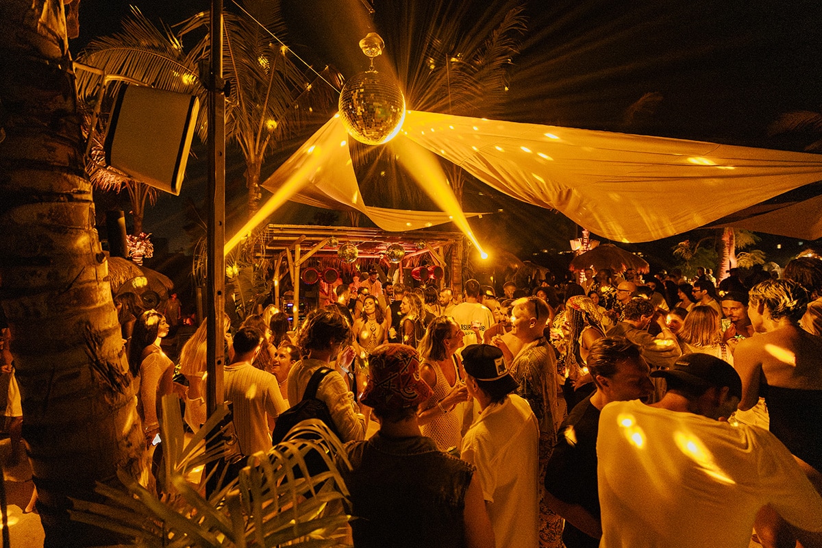 DJ HIMMAT performing at La Piscine Electronique, an open-air party with a vibrant crowd and golden disco lights, blending global sounds and mindful energy.