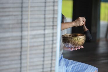 Woman practising sound healing with a Tibetan singing bowl at Knai Bang Chatt’s wellness retreat in Cambodia – blending ancient tradition with modern mindfulness.