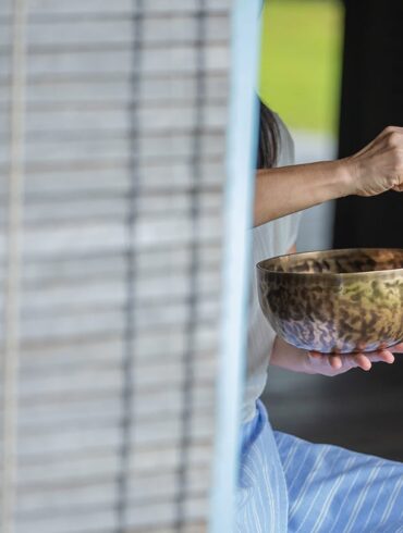 Woman practising sound healing with a Tibetan singing bowl at Knai Bang Chatt’s wellness retreat in Cambodia – blending ancient tradition with modern mindfulness.
