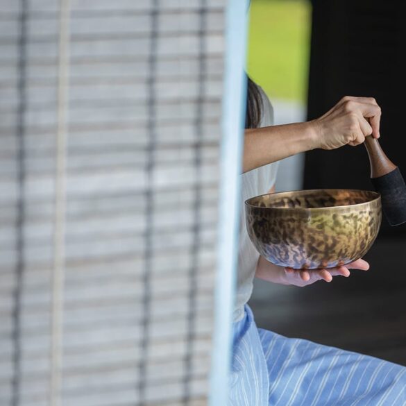 Woman practising sound healing with a Tibetan singing bowl at Knai Bang Chatt’s wellness retreat in Cambodia – blending ancient tradition with modern mindfulness.