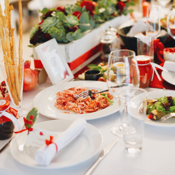 Elegant Italian Christmas Day lunch table setting with festive red-and-white decor, ribbon-wrapped napkins, fresh pomegranates, and pasta served with tomato sauce and grilled vegetables.