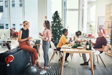 Festive office Christmas party with colleagues in holiday hats, enjoying catered food and drinks — showcasing in-office celebrations in corporate culture.