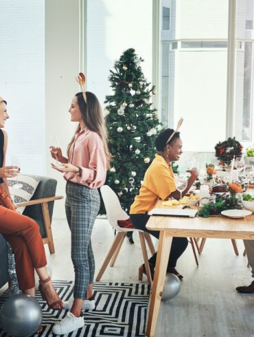 Festive office Christmas party with colleagues in holiday hats, enjoying catered food and drinks — showcasing in-office celebrations in corporate culture.