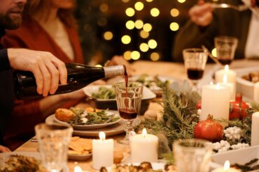 Elegant Christmas Eve dinner setting with candles, festive greenery, and a person pouring red wine at a holiday gathering table in Singapore.