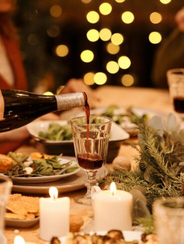 Elegant Christmas Eve dinner setting with candles, festive greenery, and a person pouring red wine at a holiday gathering table in Singapore.
