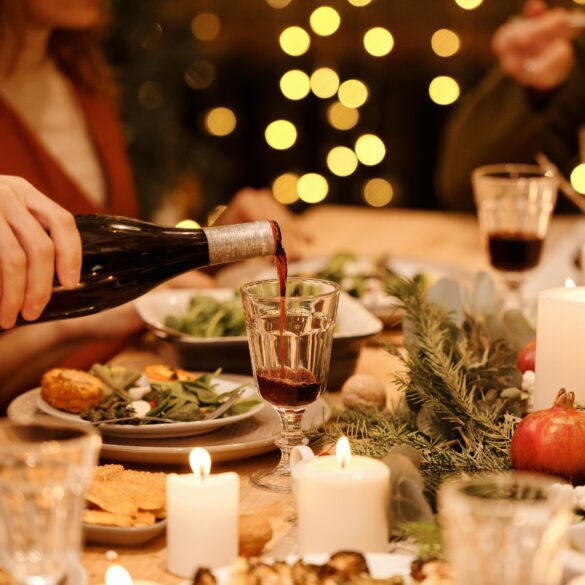 Elegant Christmas Eve dinner setting with candles, festive greenery, and a person pouring red wine at a holiday gathering table in Singapore.