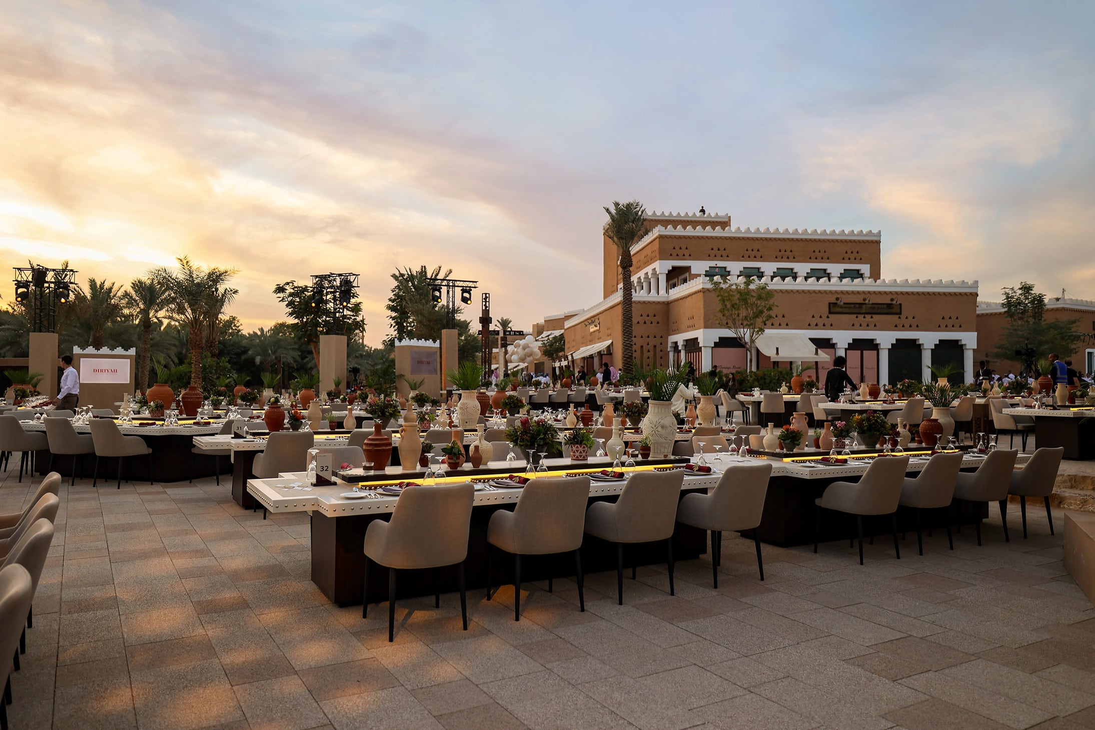 Outdoor dining setup at Bujairi Terrace in Diriyah, Saudi Arabia, featuring Najdi-style architecture and sunset views over the heritage district.
