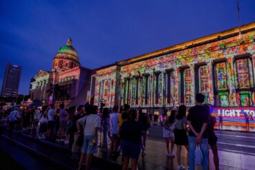 Crowds gather in front of the National Gallery Singapore during Light to Night Festival, with vibrant digital art projections lighting up the colonial facade as part of Singapore Art Week.
