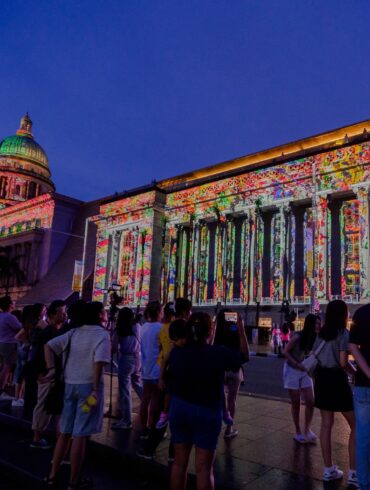 Crowds gather in front of the National Gallery Singapore during Light to Night Festival, with vibrant digital art projections lighting up the colonial facade as part of Singapore Art Week.