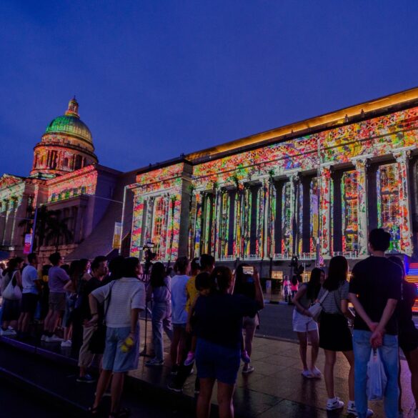 Crowds gather in front of the National Gallery Singapore during Light to Night Festival, with vibrant digital art projections lighting up the colonial facade as part of Singapore Art Week.
