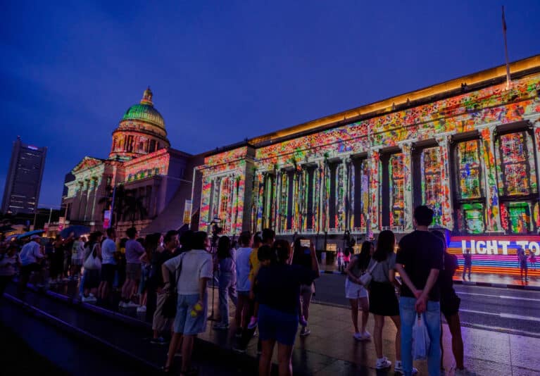 Crowds gather in front of the National Gallery Singapore during Light to Night Festival, with vibrant digital art projections lighting up the colonial facade as part of Singapore Art Week.