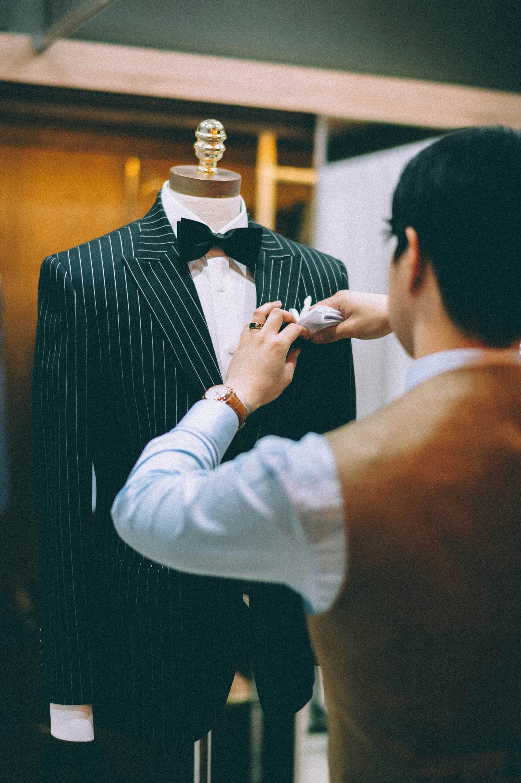 Tailor adjusting a pinstripe tuxedo on a mannequin in a bespoke suit shop, highlighting luxury custom tailoring and sartorial craftsmanship.