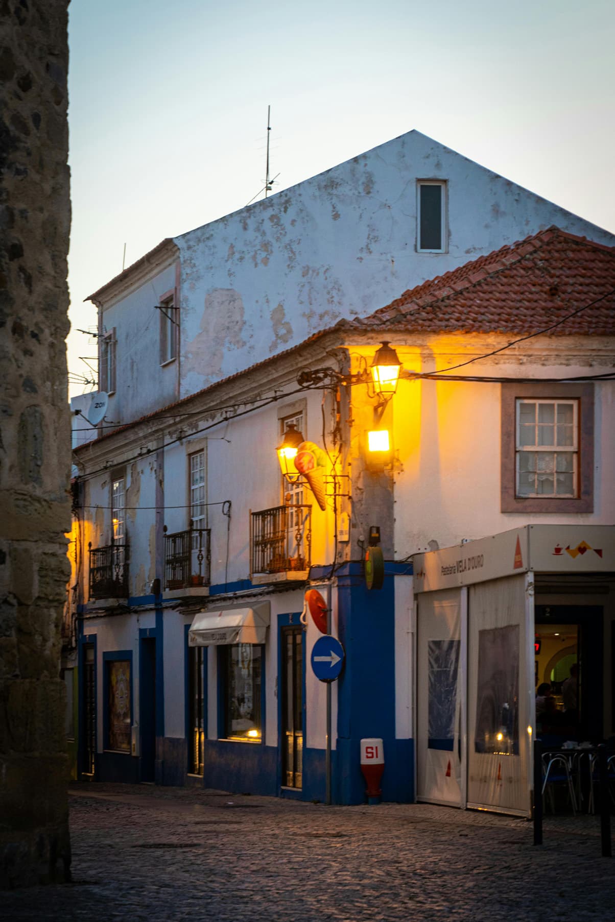 Charming cobblestone street at dusk in Sines, Portugal, with traditional whitewashed buildings and glowing street lamps — ideal for road trip explorers.