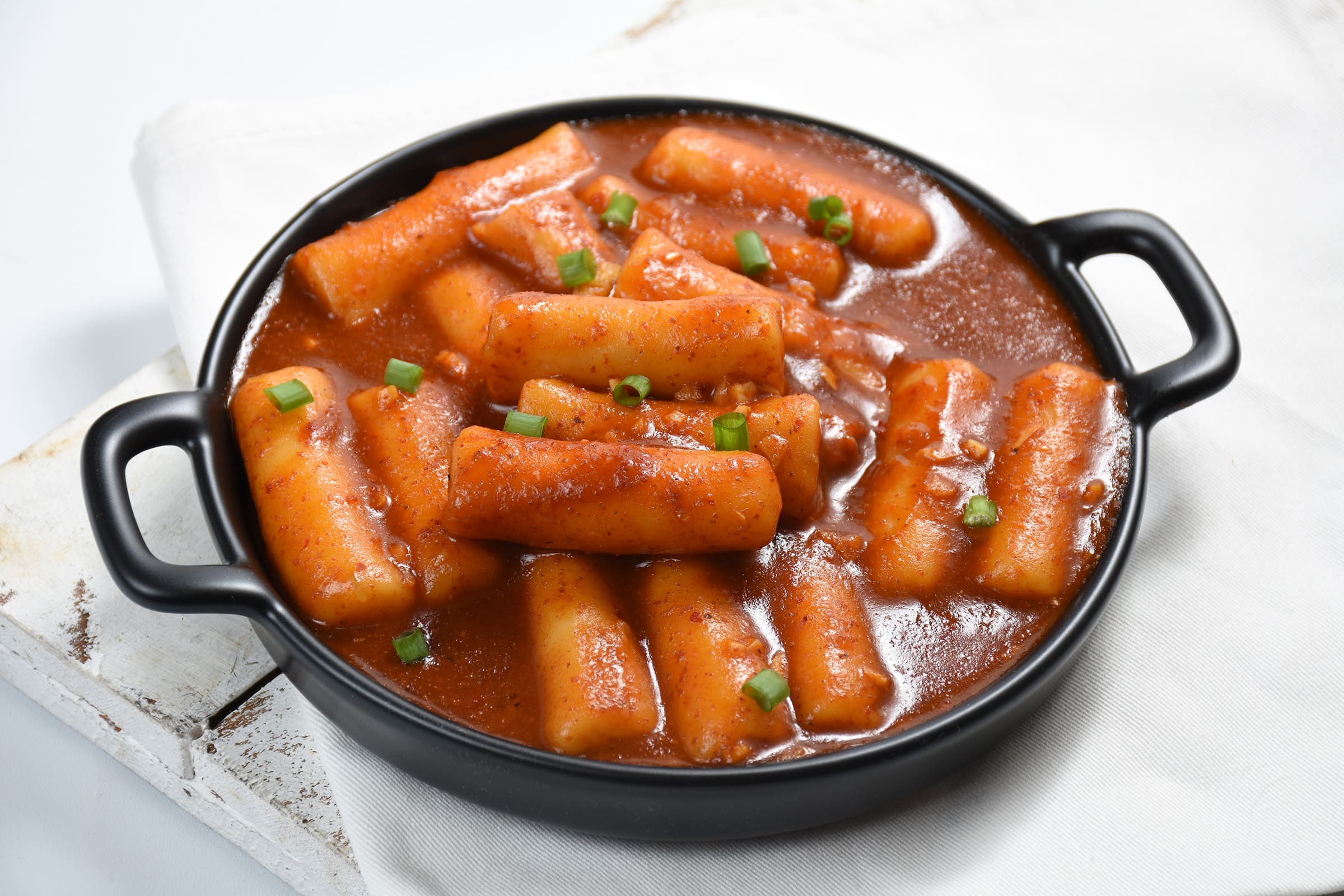Spicy Korean tteokbokki rice cakes in a rich gochujang sauce, garnished with scallions in a black serving pan.