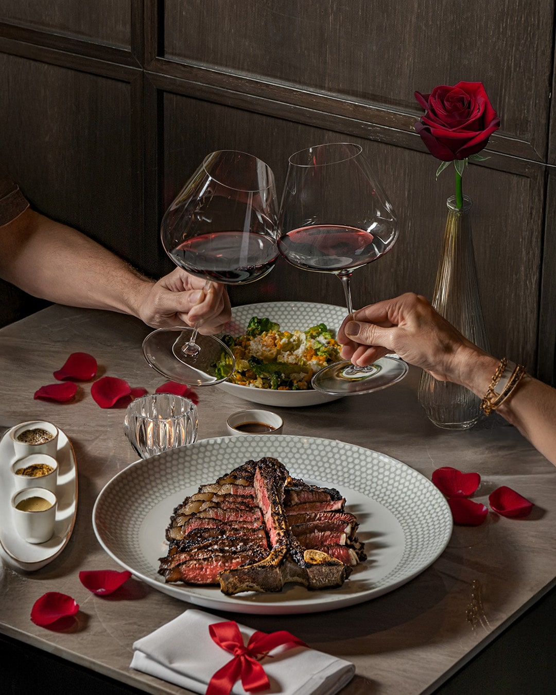 Valentine’s Day steak dinner at 54 Steakhouse in Singapore, with T-bone steak, Caesar salad, red wine, and rose petals for a romantic ambiance.