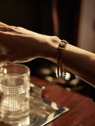 Close-up of a woman reaching for a cocktail shaker while wearing the FORNA gold cuffing bracelet — intimacy jewellery designed for subtle sensuality.