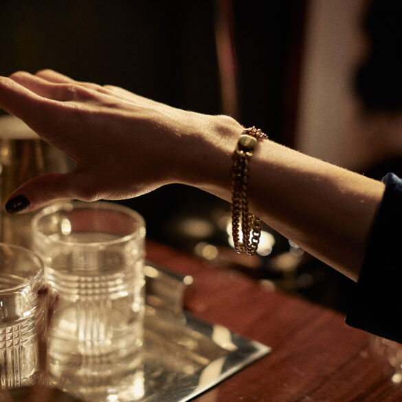 Close-up of a woman reaching for a cocktail shaker while wearing the FORNA gold cuffing bracelet — intimacy jewellery designed for subtle sensuality.