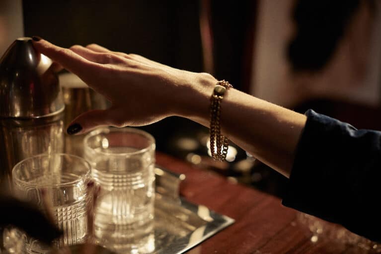 Close-up of a woman reaching for a cocktail shaker while wearing the FORNA gold cuffing bracelet — intimacy jewellery designed for subtle sensuality.
